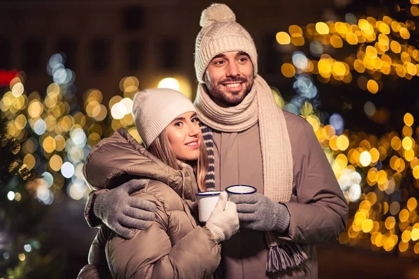 people, holidays and leisure concept - happy couple with tea cups over christmas lights