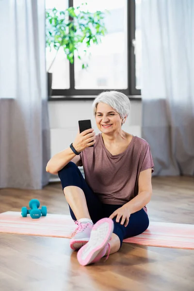 스포츠 라이프 스타일 스마트폰으로 매트에서 운동하는 나이든 여성에게 미소짓기 — 스톡 사진