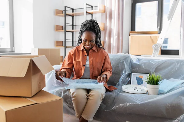 moving, people and real estate concept - happy smiling woman packing boxes sitting on sofa at home