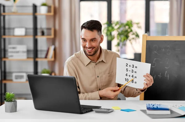 distance education, primary school and remote job concept - happy smiling male math teacher with laptop and simple mathematical equalities having online class at home office