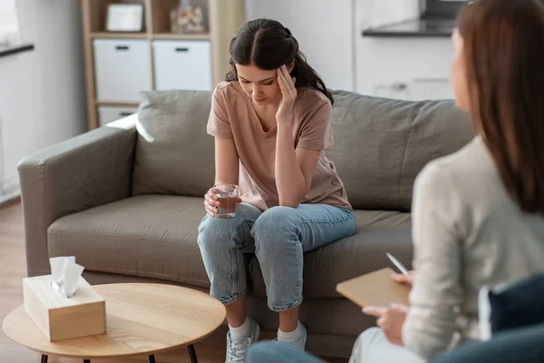 psychology, mental health and people concept - sad young woman patient with glass of water and woman psychologist at psychotherapy session