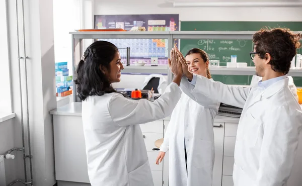 science, work and people concept - international group of happy scientists making high five gesture in laboratory