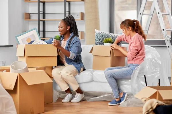 moving, people and real estate concept - women unpacking boxes at new home