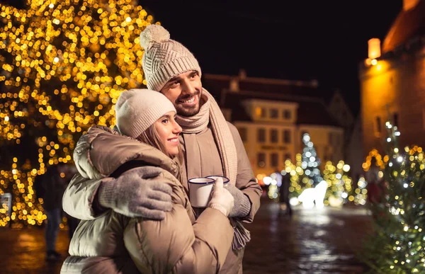 people, holidays and leisure concept - happy couple with tea cups over christmas lights in city at night