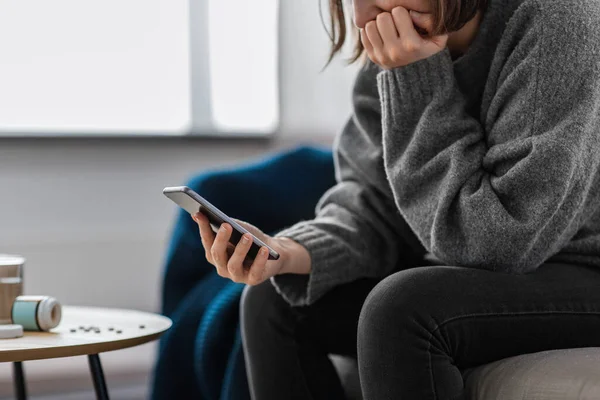 mental health, psychological help and depression concept - close up of stressed woman with medicine pills on table holding smartphone at home