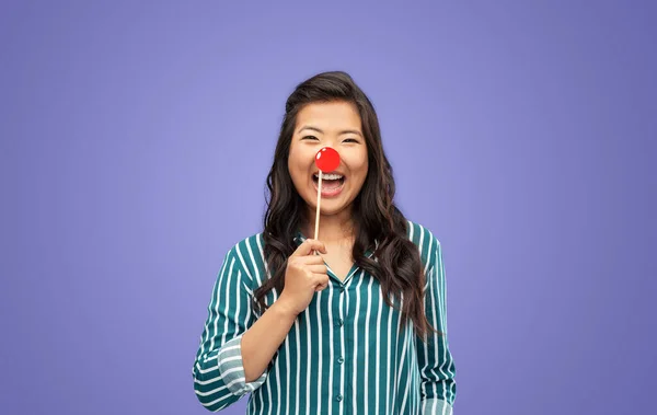 red nose day, party props and photo booth concept concept - happy woman with clown nose over violet background