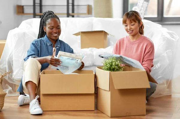 moving, people and real estate concept - women unpacking boxes at new home or packing stuff into bubble wrap