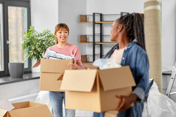 moving, people and real estate concept - happy smiling women with boxes at new home