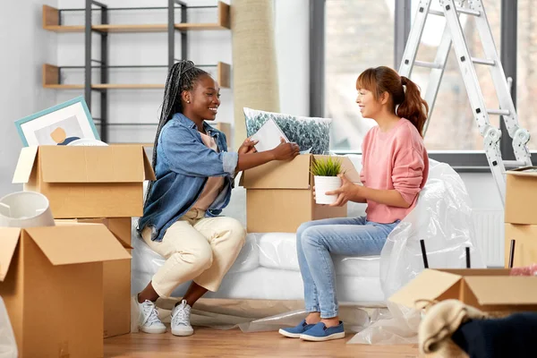 moving, people and real estate concept - women unpacking boxes at new home