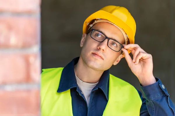 construction business and building concept - male builder in helmet and glasses looking up