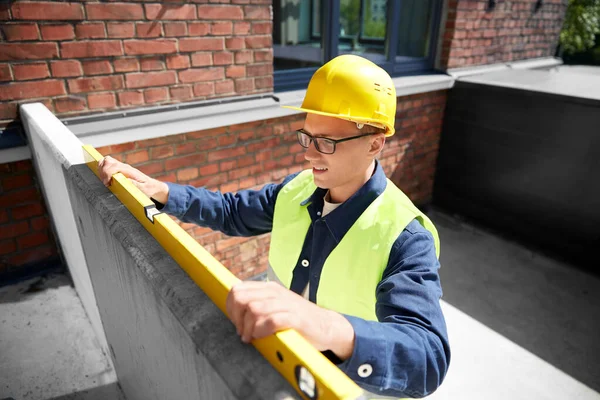 construction business and building concept - male builder with level measuring wall