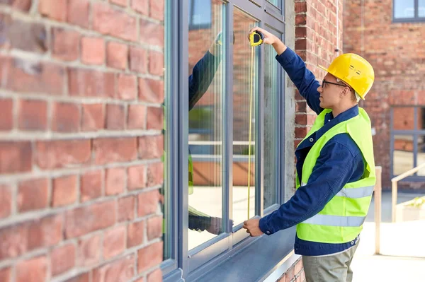 construction business and building concept - male builder with ruler measuring window