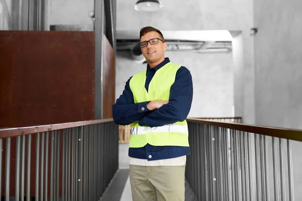 architecture, construction business and building concept - happy smiling male worker in safety west at office