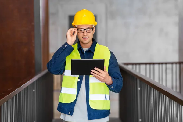 architecture, construction business and building concept - happy smiling male architect in helmet and safety west with tablet pc computer at office