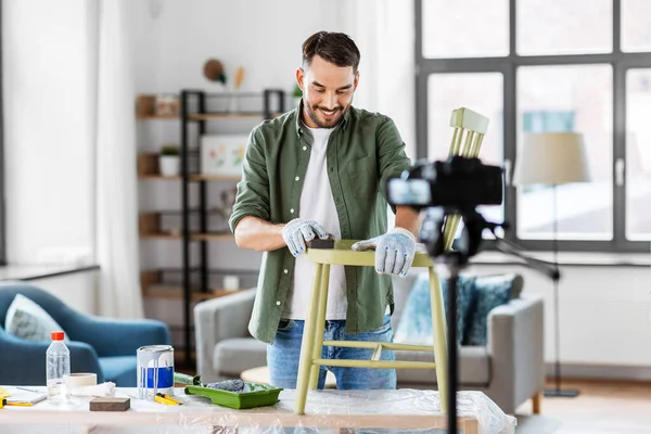 blogging, furniture restoration and home improvement concept - happy smiling man or blogger with camera sanding old wooden chair with sponge and recording tutorial video