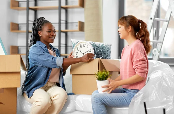 moving, people and real estate concept - women unpacking boxes at new home