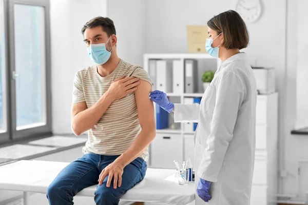 health, medicine and pandemic concept - female doctor or nurse in protective medical mask and gloves disinfecting male patients skin at hospital