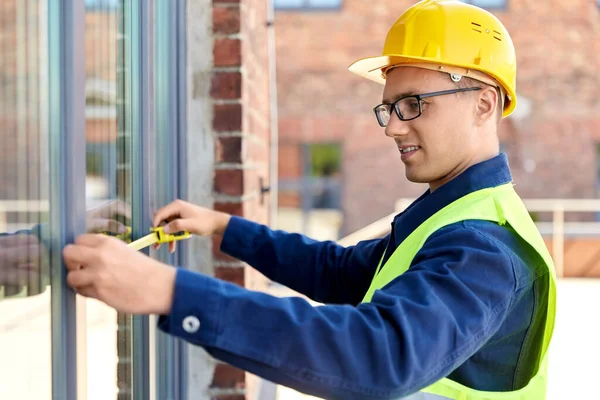 construction business and building concept - happy smiling male builder with ruler measuring window