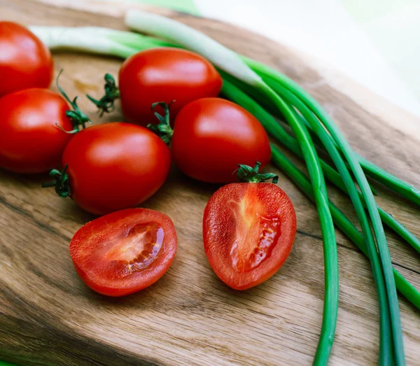 Røde tomater og grønn løk på nedskjæringstavlen – stockfoto