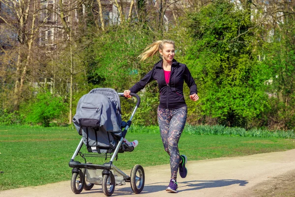 Lachende vrouw duwen baby buggy — Stockfoto