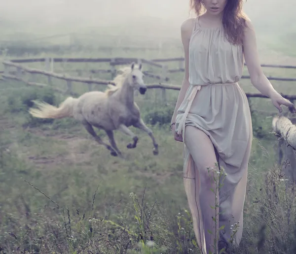 Delicate brunette posing with horse in the background — Stock Photo, Image