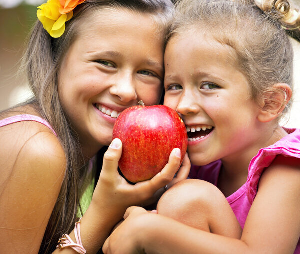 Two sisters sharing a big red apple