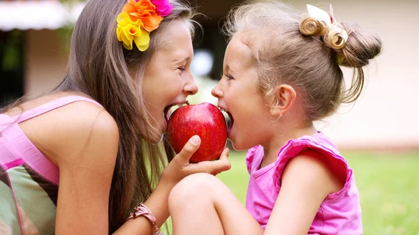 Sweet red apple being bitten by sisters — Stock Photo, Image