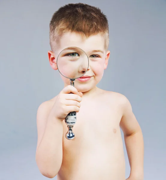 Beautiful little boy looking through a magnifying glass — Stock Photo, Image