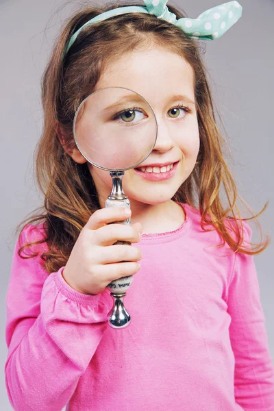 Schönes kleines Mädchen, das durch ein Vergrößerungsglas schaut — Stockfoto