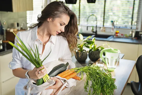 袋から野菜を選別し キッチンテーブルの上に置く良い気分で美しい若い女性 — ストック写真