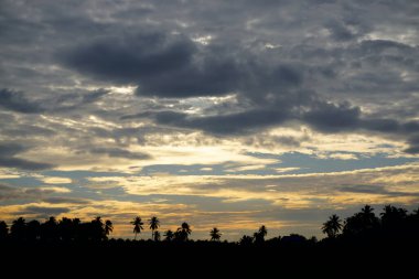 Gün batımının görüntüsü gökyüzünde bulutlar ve manzara ön planında siluet