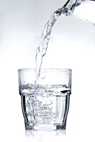 Наполнение стакана водой на светло-голубом фоне — стоковое фото