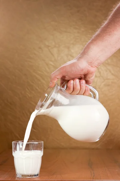 Hand pouring milk from jug to glass — Stock Photo, Image