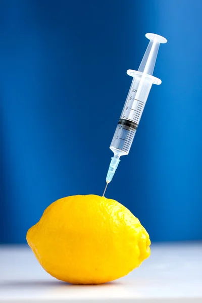 Syringe stuck in lemon over blue background — Stock Photo, Image