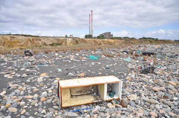 Trashed fridge on the seashore next to a factory — Stock Photo, Image