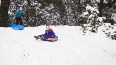 Cute kids sledding and having fun in the snow. A small child slides quickly on a sled. Screaming with joy. It's a bright winter day.