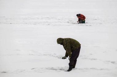 Winter fishing from the ice on the lake (reservoir) on a cold day. warmly dressed fishermen