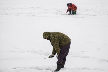 Winter fishing from the ice on the lake (reservoir) on a cold day. warmly dressed fishermen