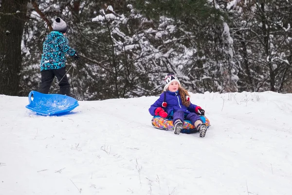 Cute kids sledding and having fun in the snow. A small child slides quickly on a sled. Screaming with joy. It's a bright winter day.