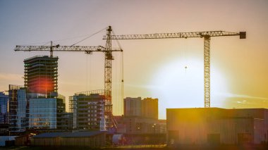 Bina. İnşaat vinçleri, gökdelenler. Gün batımında siluetler