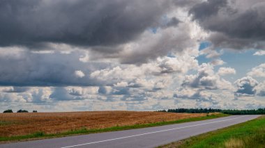 Kırsal yol ufuktan geçiyor. Tarlanın üzerinde fırtına bulutları.