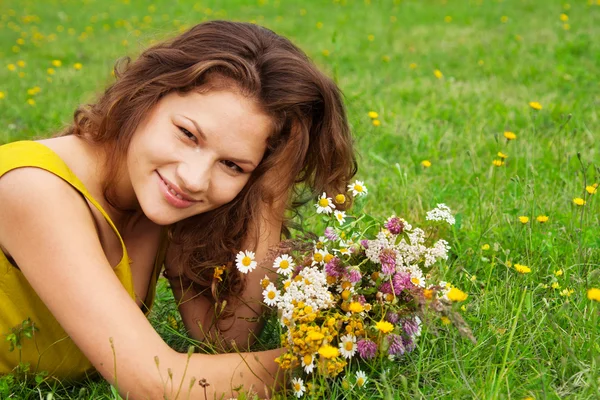Beautiful girl laying on grass with bouquet — Stock Photo, Image