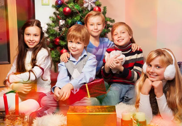 Niedliche Kinder sitzen am Weihnachtsbaum Stockfoto