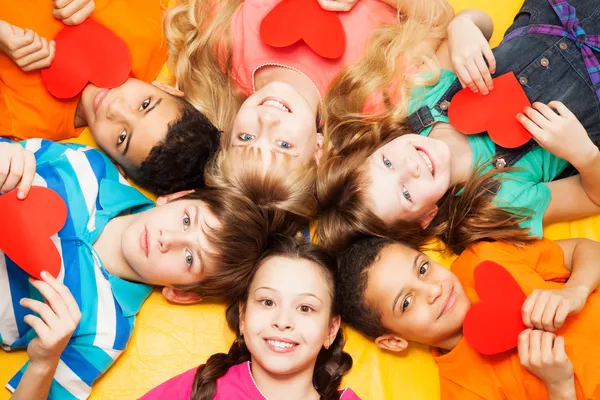 Kids laying in circle with hearts in their hands — Stock Photo, Image