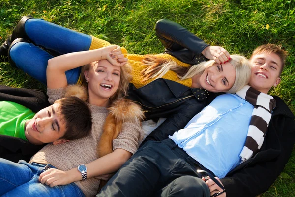 Grupo de quatro jovens deitado na grama — Fotografia de Stock