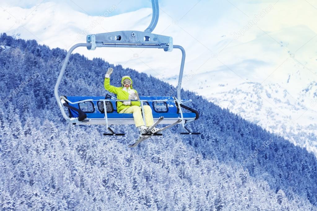 Happy skier in on the ski lift waiving hand