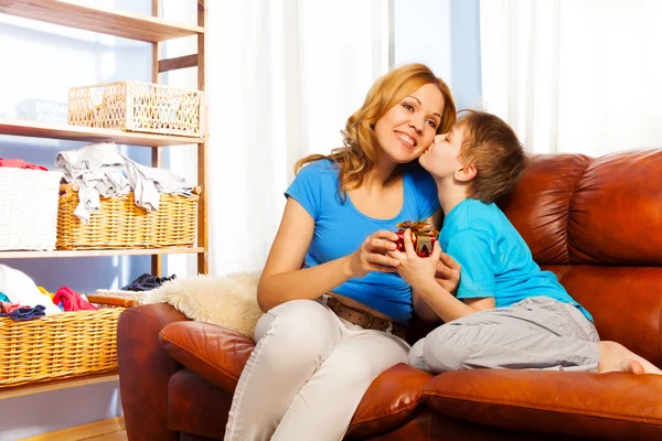 Boy is kissing his mother in cheek and giving gift to her — Stock Photo, Image