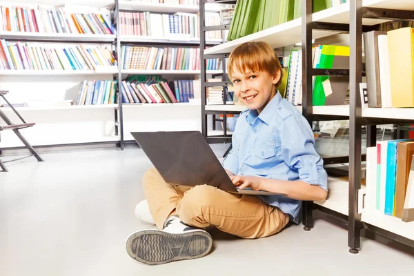 Chlapec s notebookem v knihovně — Stock fotografie