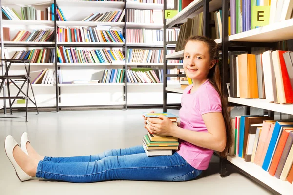 Mädchen sitzt neben Bücherregal — Stockfoto