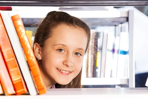 Girl looks through bookshelf — Stock Photo, Image